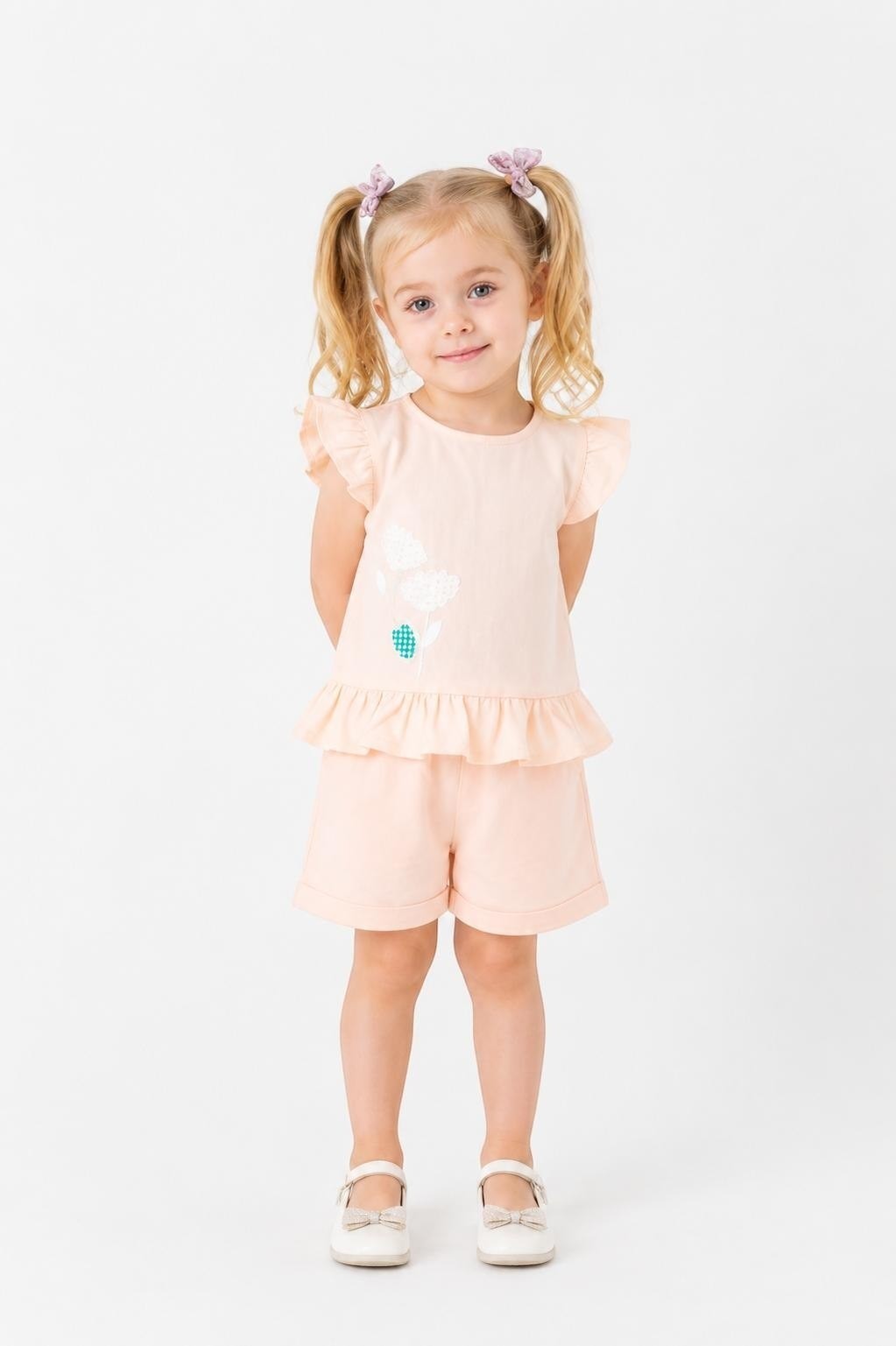 Toddler girl wearing a peach The Nile Luxuries peplum top with flutter sleeves and matching shorts with floral detail.