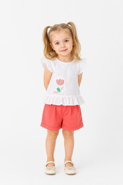 Toddler girl wearing The Nile Luxuries white peplum top with floral graphic and coral shorts on a white background.
