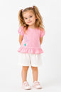 Toddler girl wearing a pink peplum top with puff sleeves and floral detail and white shorts by The Nile Luxuries