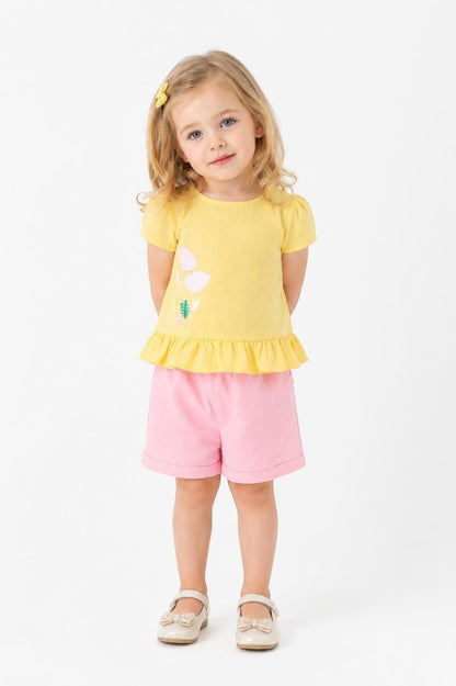Toddler girl wearing a yellow peplum top with floral graphic and pink shorts by The Nile Luxuries.