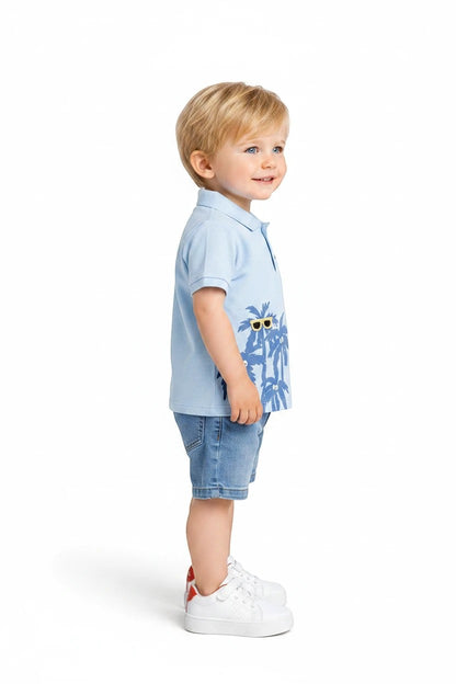 Toddler boy wearing The Nile Luxuries light blue palm tree polo shirt and denim shorts set with white sneakers.