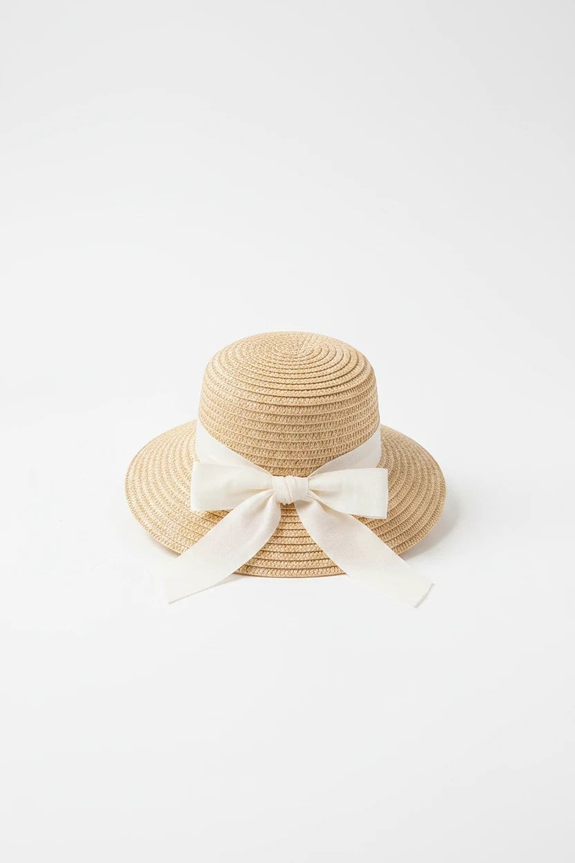 The Nile Luxuries toddler sun hat in woven straw with a white ribbon bow, perfect for summer outdoor protection.