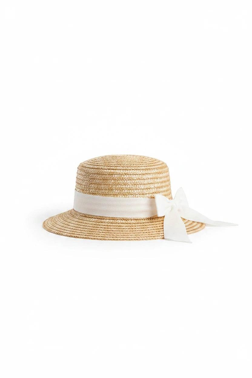 The Nile Luxuries toddler sun hat in woven straw with a white ribbon bow detail for summer sun protection.