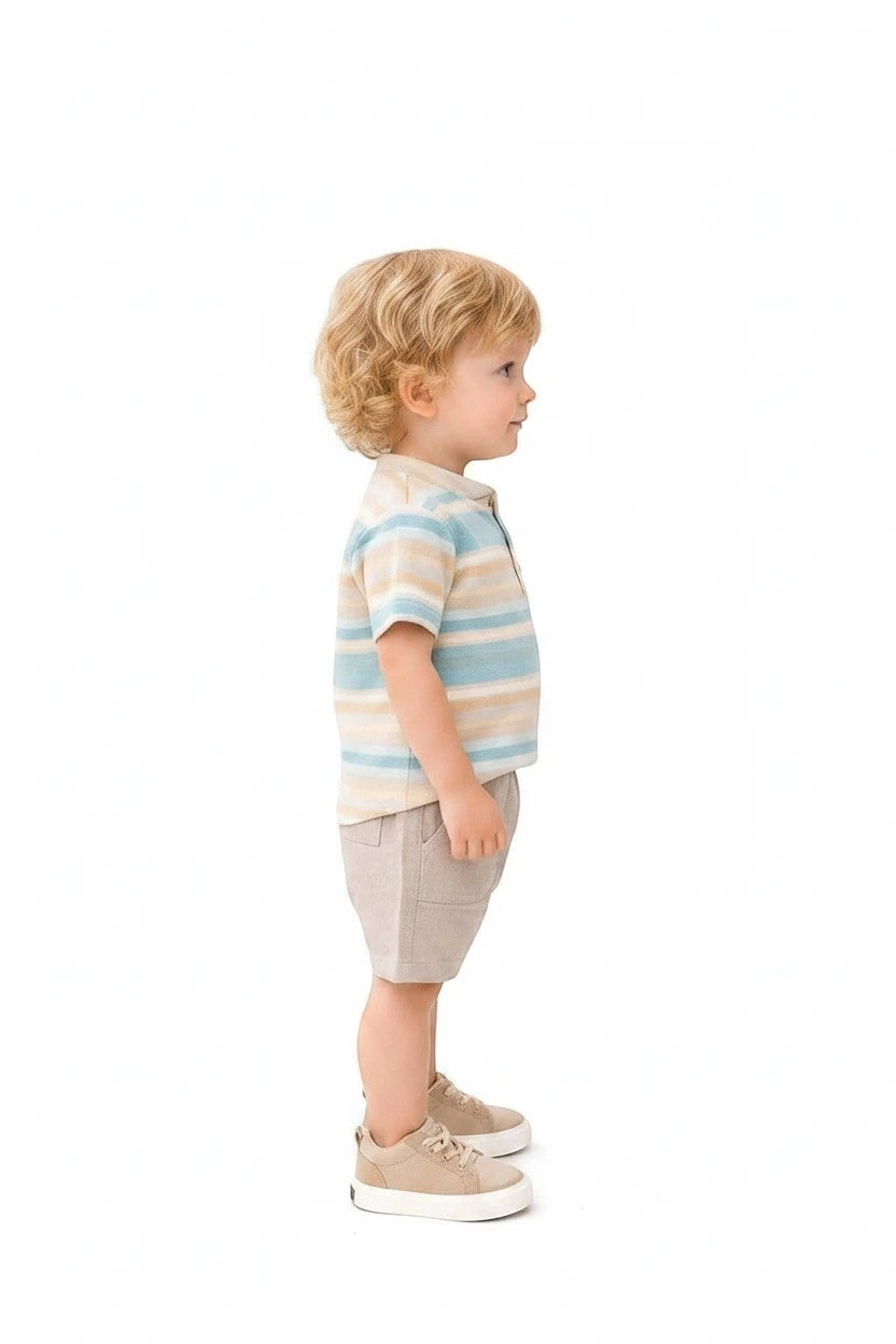 Toddler boy wearing The Nile Luxuries striped henley shirt and beige shorts with matching sneakers on white background