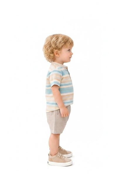 Toddler boy wearing The Nile Luxuries striped henley shirt and beige shorts with matching sneakers on white background