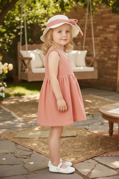 Toddler girl wearing a The Nile Luxuries sleeveless dusty pink dress and matching sun hat with a bow in a garden.