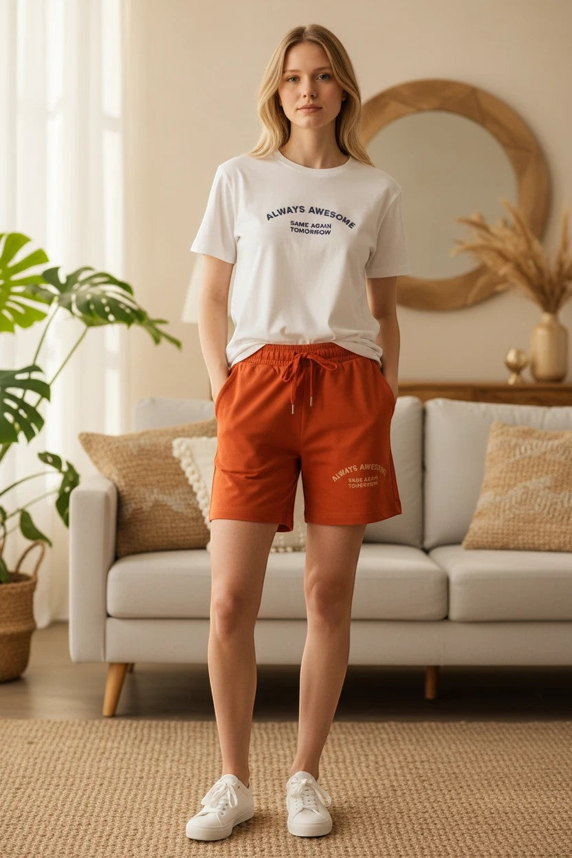 The Nile Luxuries white graphic t-shirt and rust orange drawstring shorts lounge set worn by a woman indoors.