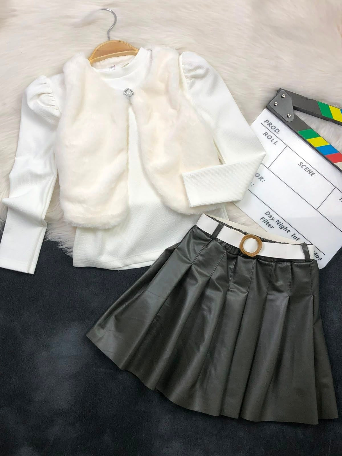 The Nile Luxuries three-piece youth outfit with a white ribbed top, plush faux-fur vest, and grey pleated leather skirt.
