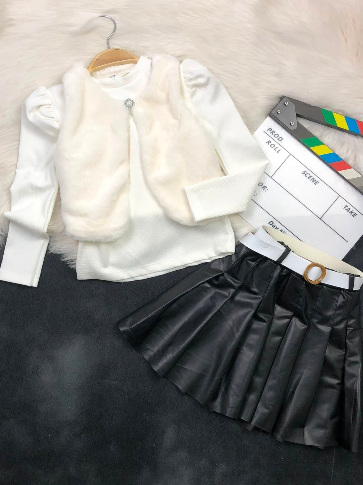 The Nile Luxuries three-piece youth outfit with a white ribbed top, plush faux-fur vest, and black pleated skirt.