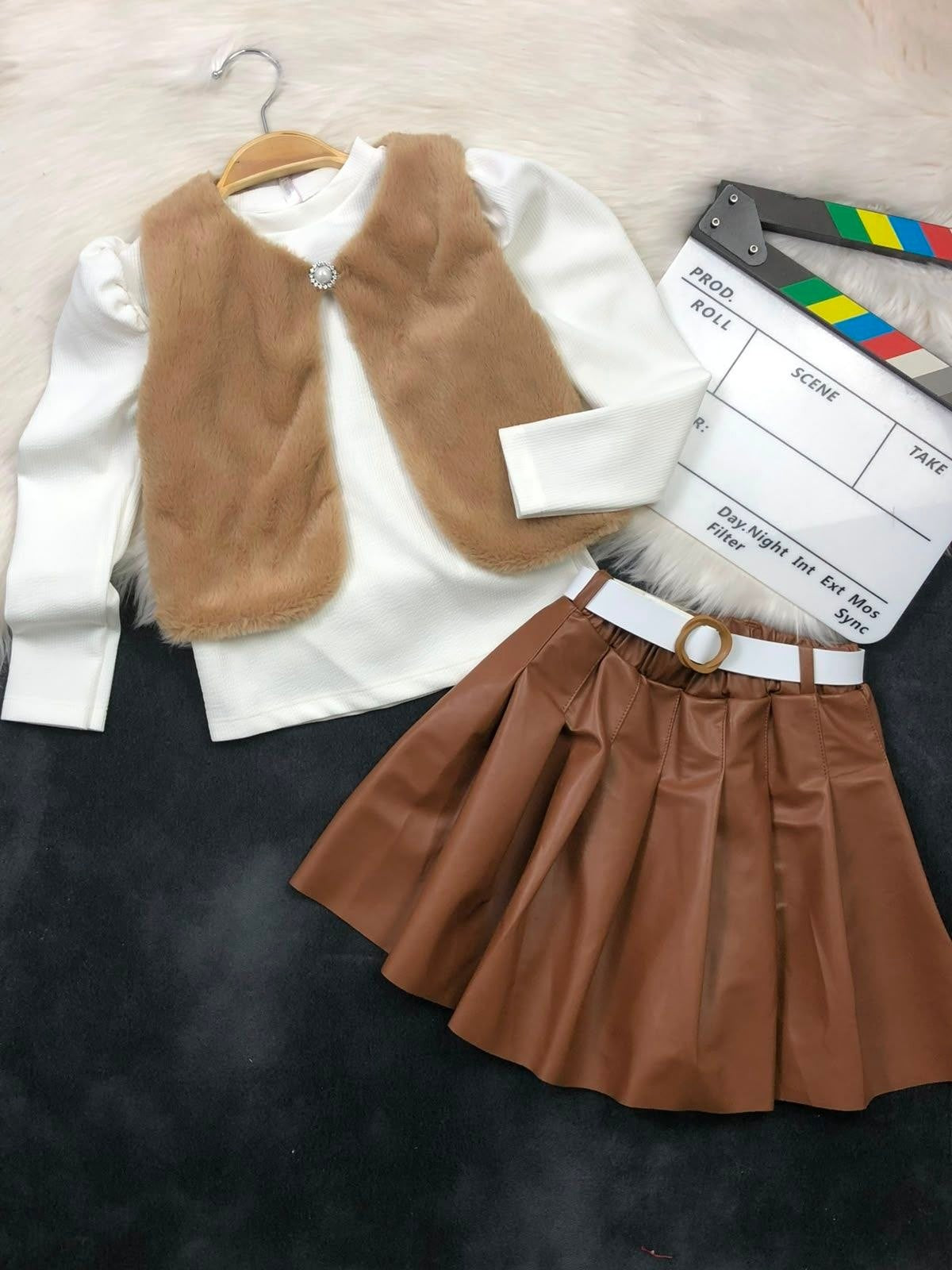 The Nile Luxuries three-piece youth outfit with a white ribbed top, brown faux-fur vest, and pleated faux-leather skirt.