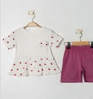 The Nile Luxuries baby girls white short-sleeve tunic with red heart print and peplum hem, paired with plum shorts. Ribbed fabric.