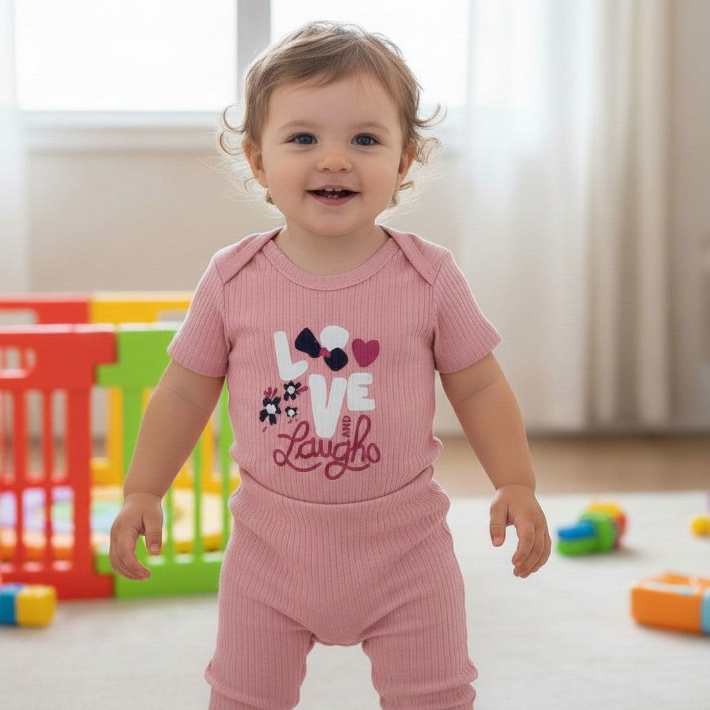 The Nile Luxuries baby pink ribbed knit bodysuit with "LOVE and Laugh" graphic and light blue shorts.