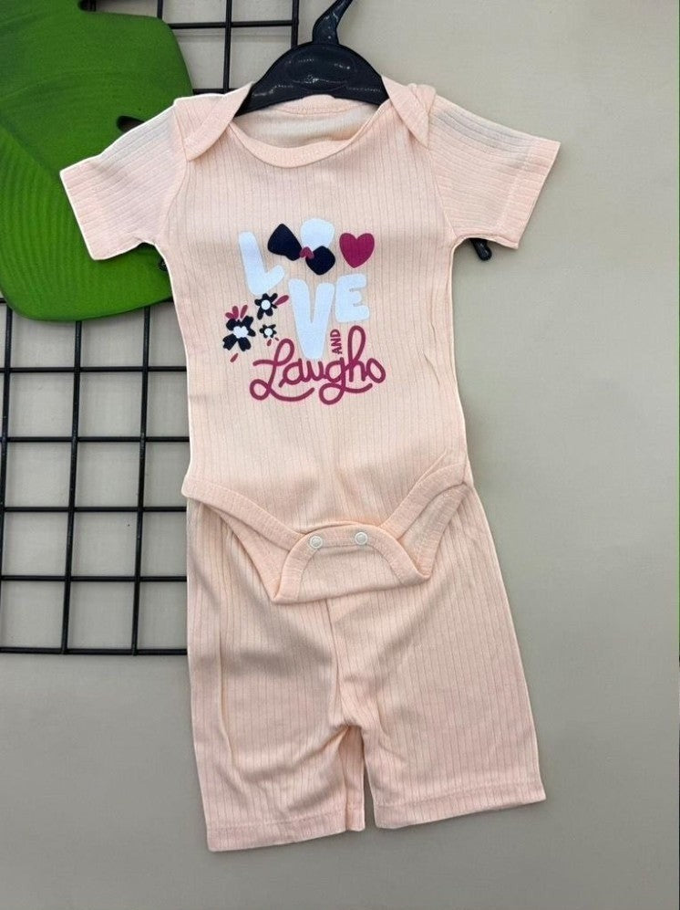 The Nile Luxuries baby ribbed knit bodysuit and shorts set in peach with "LOVE and Laugh" graphic, bow, hearts, and flowers.
