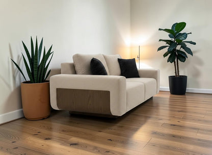 The Nile Luxuries modern beige fabric sofa with wooden side accents and black decorative pillows.