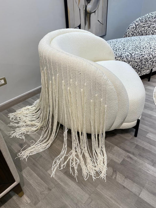 The Nile Luxuries creamy off-white boucle armchair with dramatic fringe detailing and black legs.