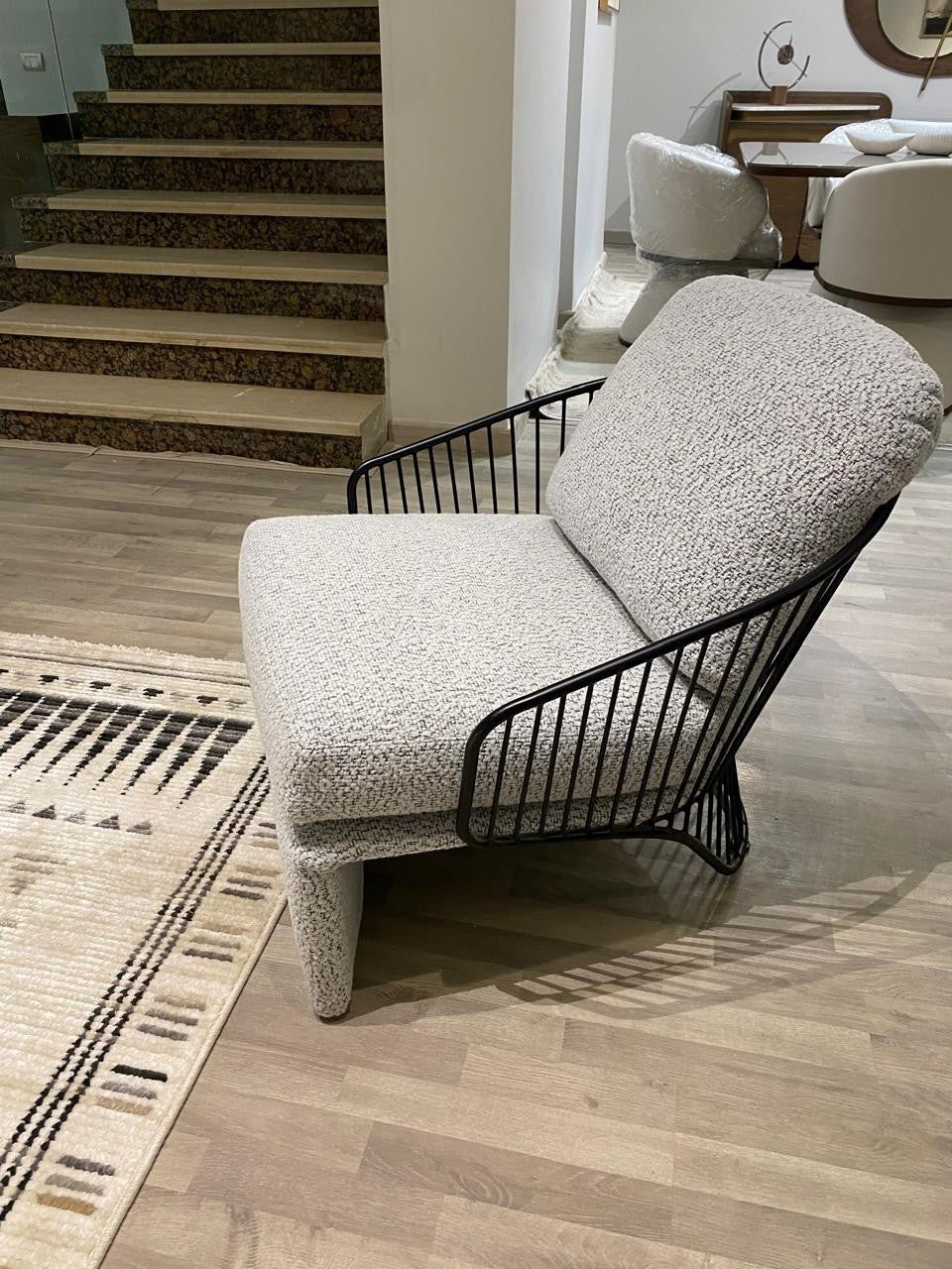 The Nile Luxuries modern light grey boucle armchair with black metal frame and cage-like arms.
