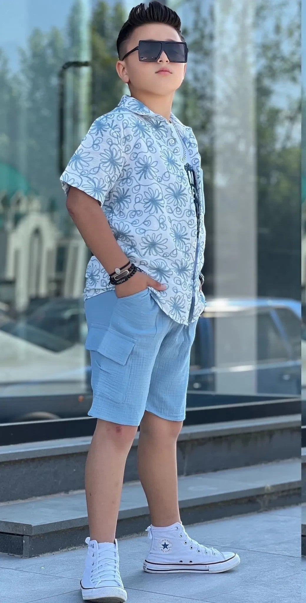 The Nile Luxuries boys' light blue printed short sleeve button-up shirt and cargo shorts set with white high-top sneakers.