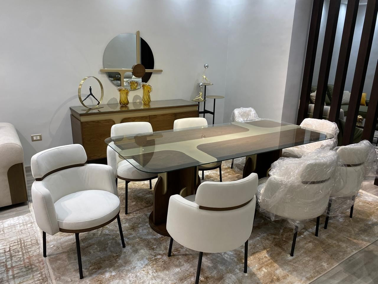 The Nile Luxuries cream fabric dining chairs with wood trim and black metal legs, surrounding a glass top table.