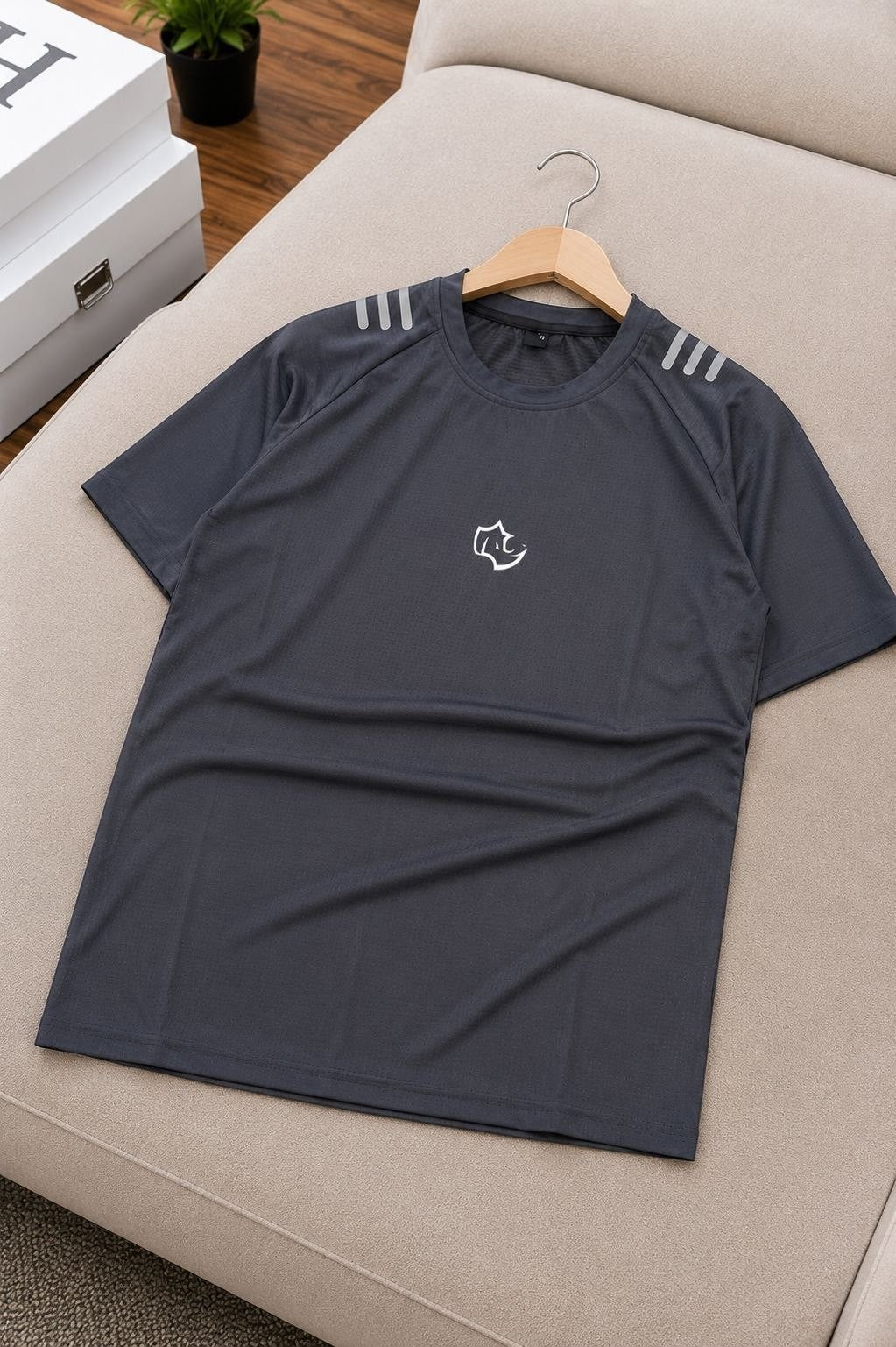 The Nile Luxuries dark grey athletic t-shirt with reflective shoulder stripes and a small white logo graphic.