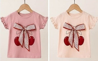 The Nile Luxuries Girls cherry print short sleeve t-shirt with ruffled sleeves and a bow accent. Available in pink and peach.