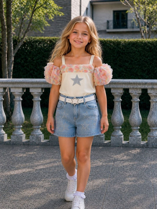 The Nile Luxuries girls' off-shoulder top with floral sleeves and star embellishment, paired with light-wash denim shorts adorned with stars.