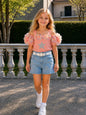 The Nile Luxuries girls' coral off-shoulder top with floral sleeves and star embellishment, paired with light-wash denim shorts.