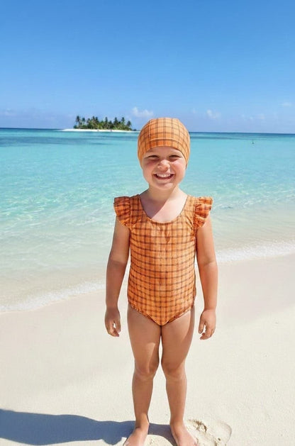 The Nile Luxuries girls orange plaid swimsuit with ruffle sleeves and matching bonnet on a beach.