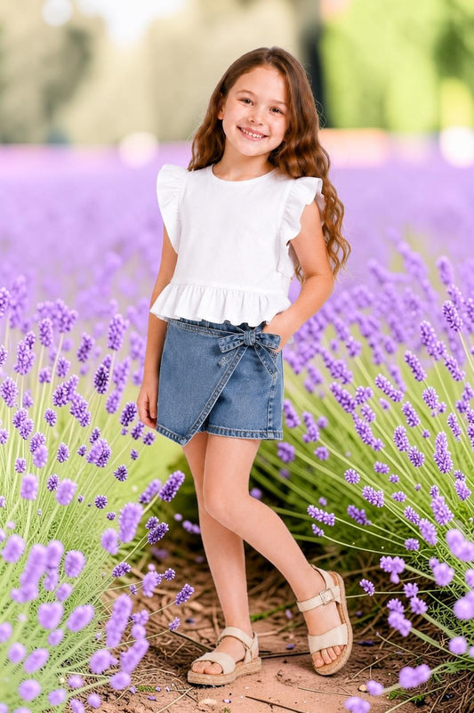The Nile Luxuries girls white cotton ruffled sleeve peplum top and denim skort set with bow detail.