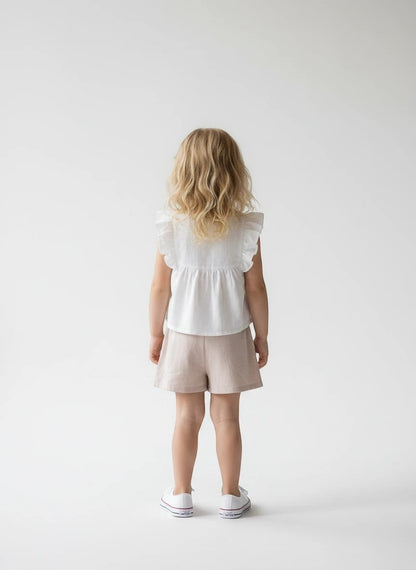 The Nile Luxuries girls' white ruffled sleeve top with floral embroidery and beige pleated shorts.