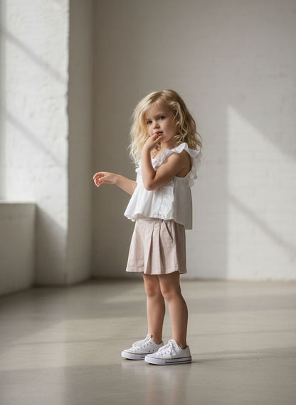 The Nile Luxuries girls' white ruffled sleeve top with floral embroidery and beige pleated shorts.