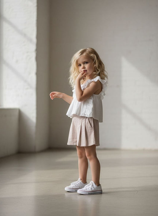 The Nile Luxuries girls' white ruffled sleeve top with floral embroidery and beige pleated shorts.