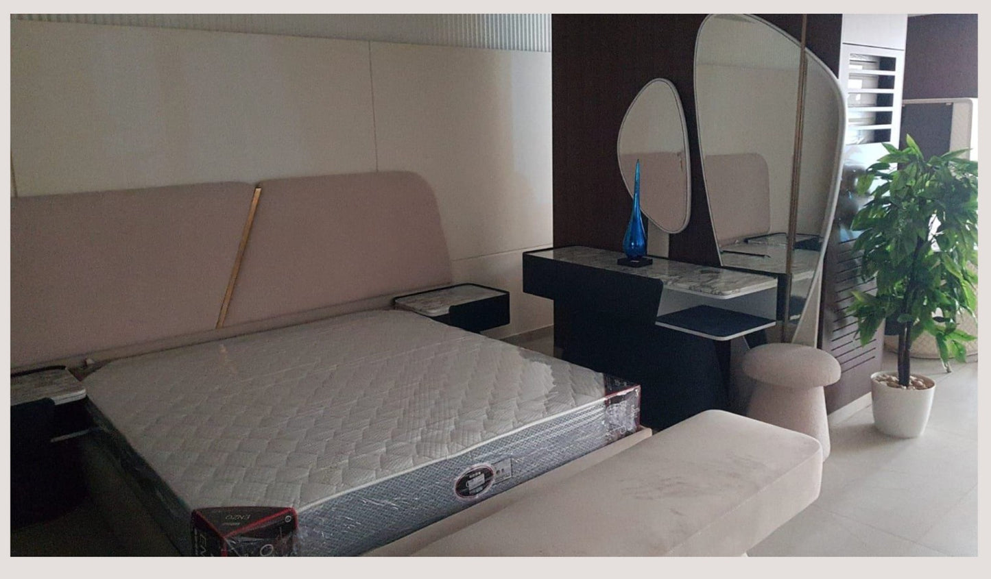 The Nile Luxuries upholstered bed frame with sculpted headboard in soft beige and gold accent. Modern bedroom set.