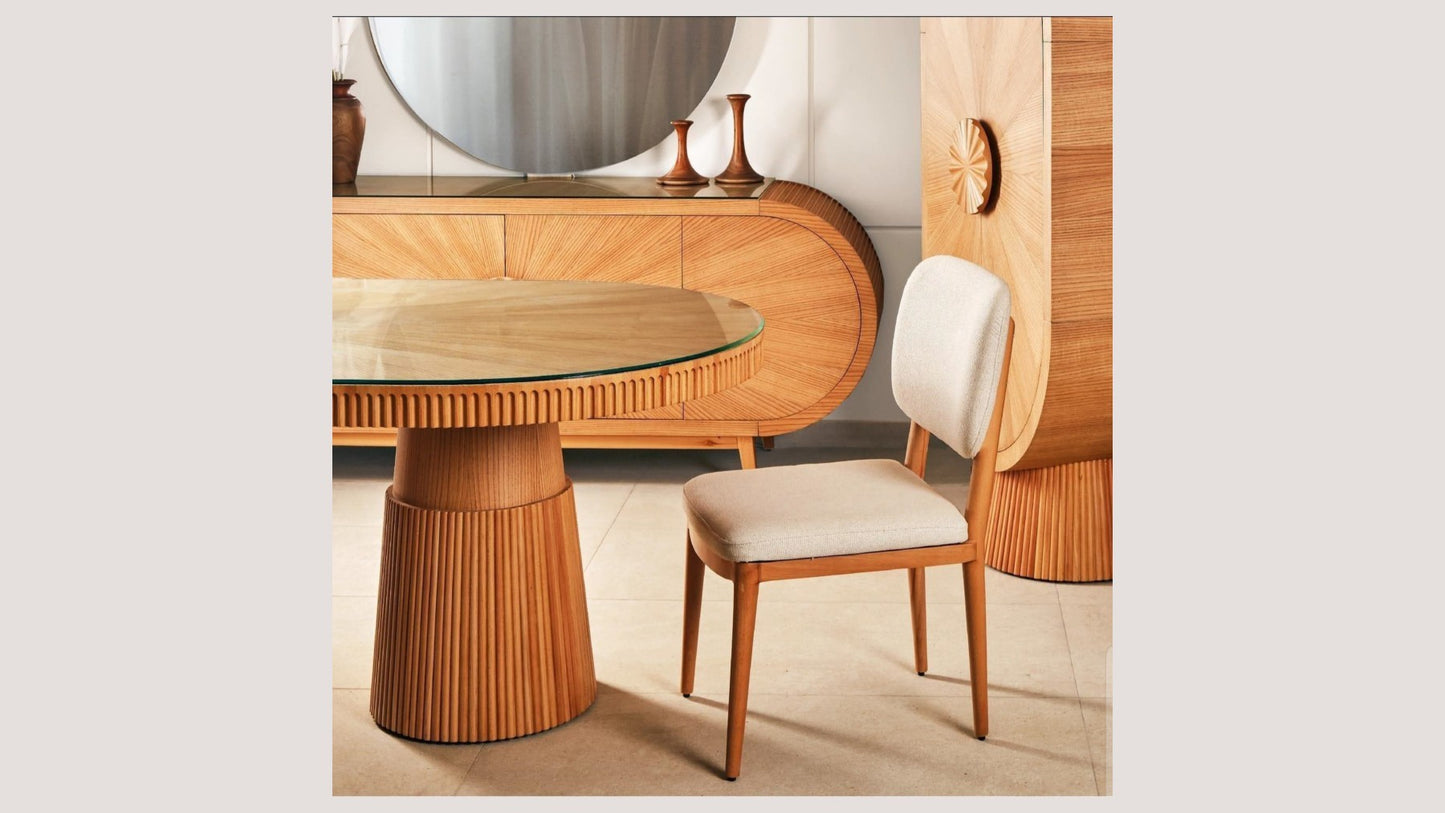 The Nile Luxuries oval dining table with fluted wood base and clear glass top, paired with a cream upholstered chair.