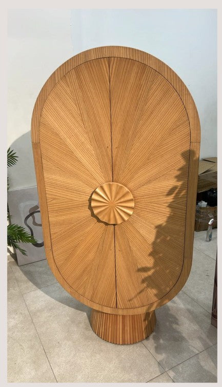 The Nile Luxuries oval wood cabinet with fluted base and sunburst wood grain detail. Features a round decorative handle.