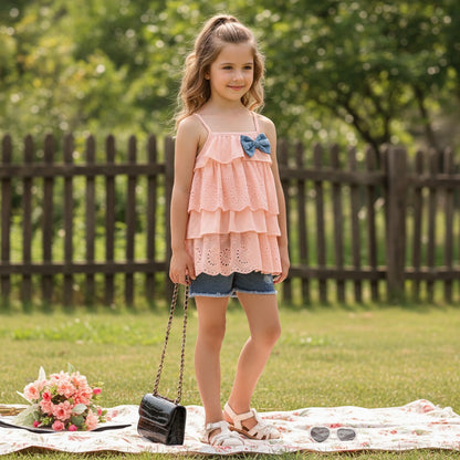 The Nile Luxuries peach eyelet ruffle tank top with denim shorts and a blue bow accent.