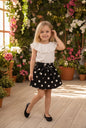 The Nile Luxuries girls' white ruffled top with black polka dot skirt, bow waist, and black ballet flats.