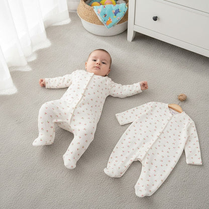 The Nile Luxuries cream ribbed knit baby sleepsuit with cherry pattern and integrated footies. A baby wears one, another hangs on a hanger.