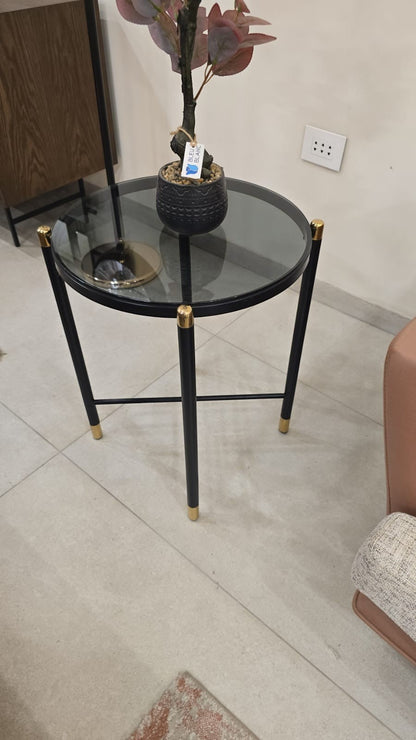 The Nile Luxuries round accent table with smoked glass top and black metal legs with gold accents.