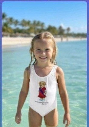The Nile Luxuries white one-piece swimsuit for girls with a graphic teddy bear wearing a red dress and blue sash.